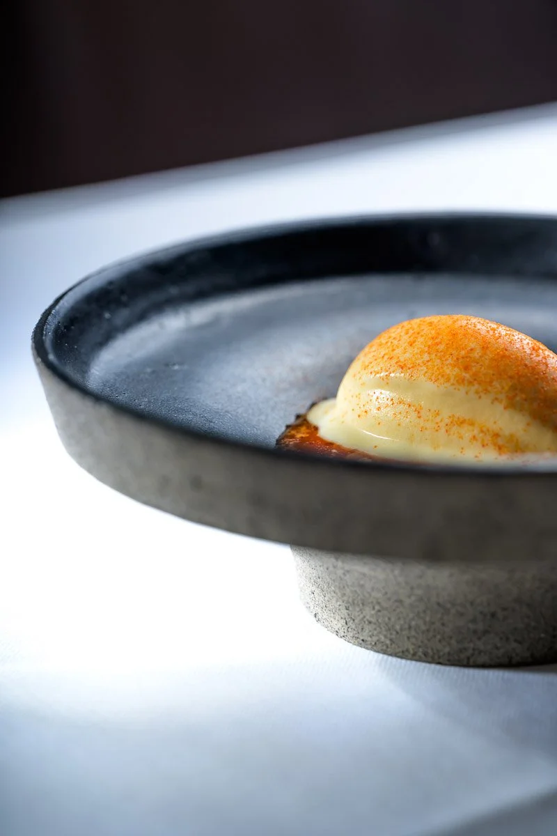 A round gray bowl with a smooth interior, containing a dollop of cream or custard topped with a reddish-orange spice, possibly paprika or cinnamon.