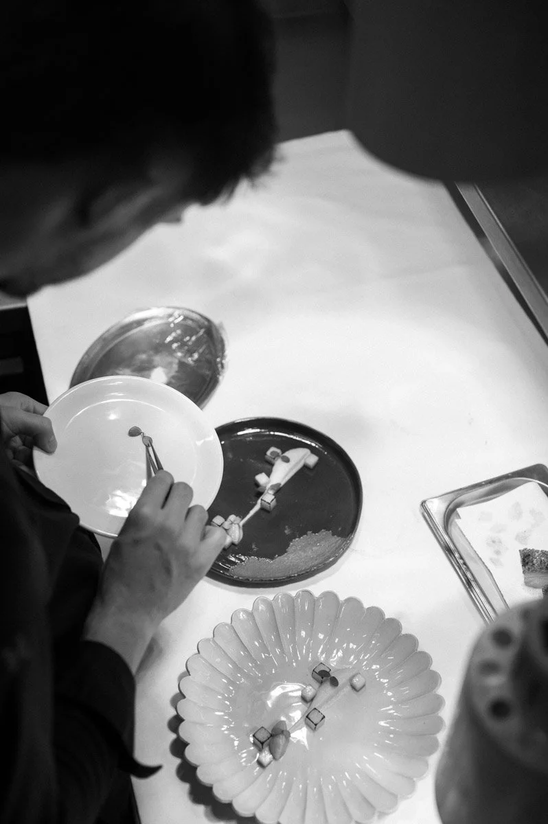 A person preparing pills or capsules on a table with plates and a tray, possibly for medication or supplement packaging.
