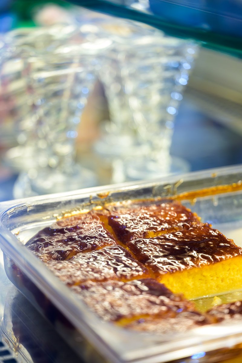 Close-up of a container with caramel flan dessert with caramelized sugar on top, with blurry glasses in the background.