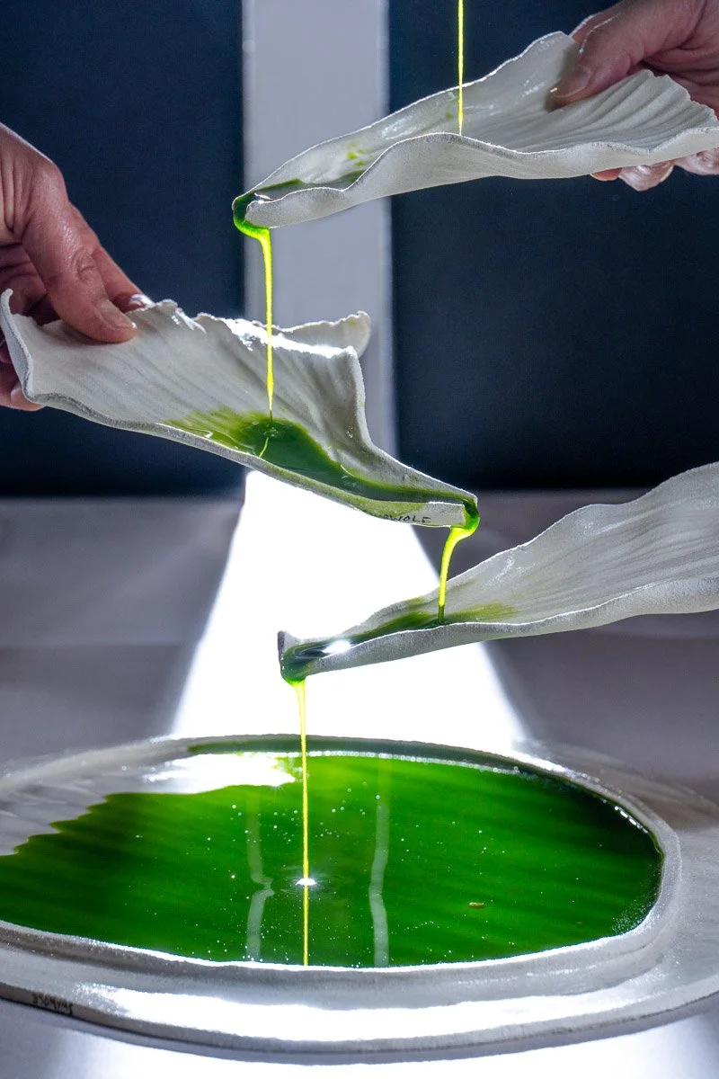Close-up of hands holding fabric sheets with green liquid being dripped onto a surface below.