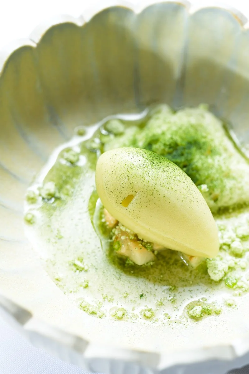 Close-up of a matcha flavored dessert with a scoop of green tea ice cream, topped with green powder, served in a metallic bowl.