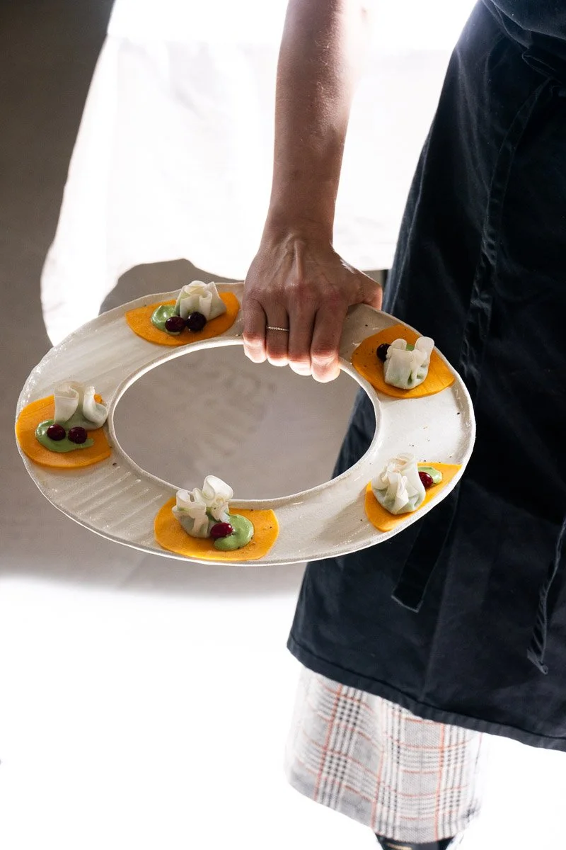 A person holding a decorative plate with small garnished appetizers or desserts, featuring white, green, and red toppings.