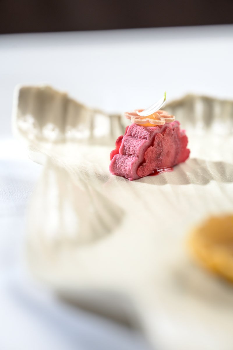 Close-up of a pink ice cream sandwich on a beige paper tray with a small decorative flower on top.