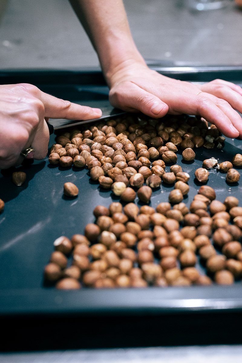 A person processing hazelnuts on a black surface, using a knife to crush or chop them.