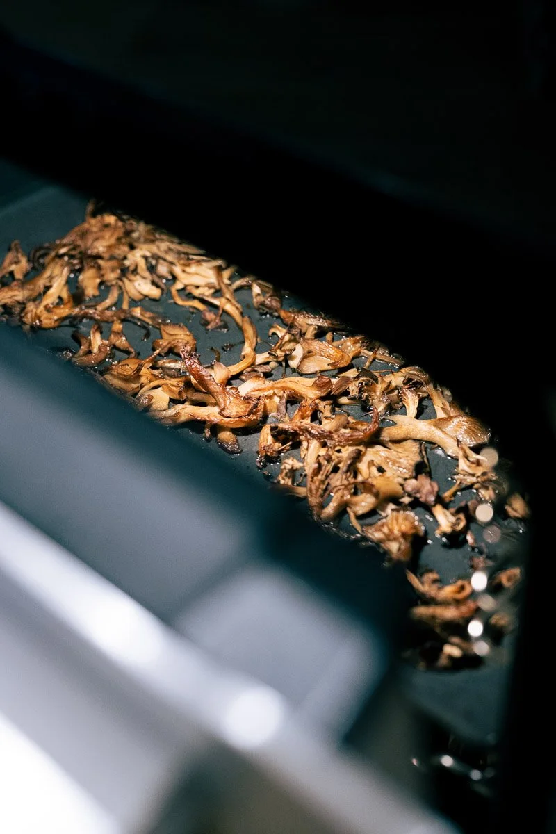 Shredded cooked mushrooms roasting on a black baking sheet inside an oven.