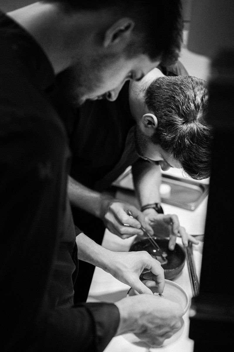 Three men preparing sushi in a kitchen, focusing on their hands as they handle ingredients.