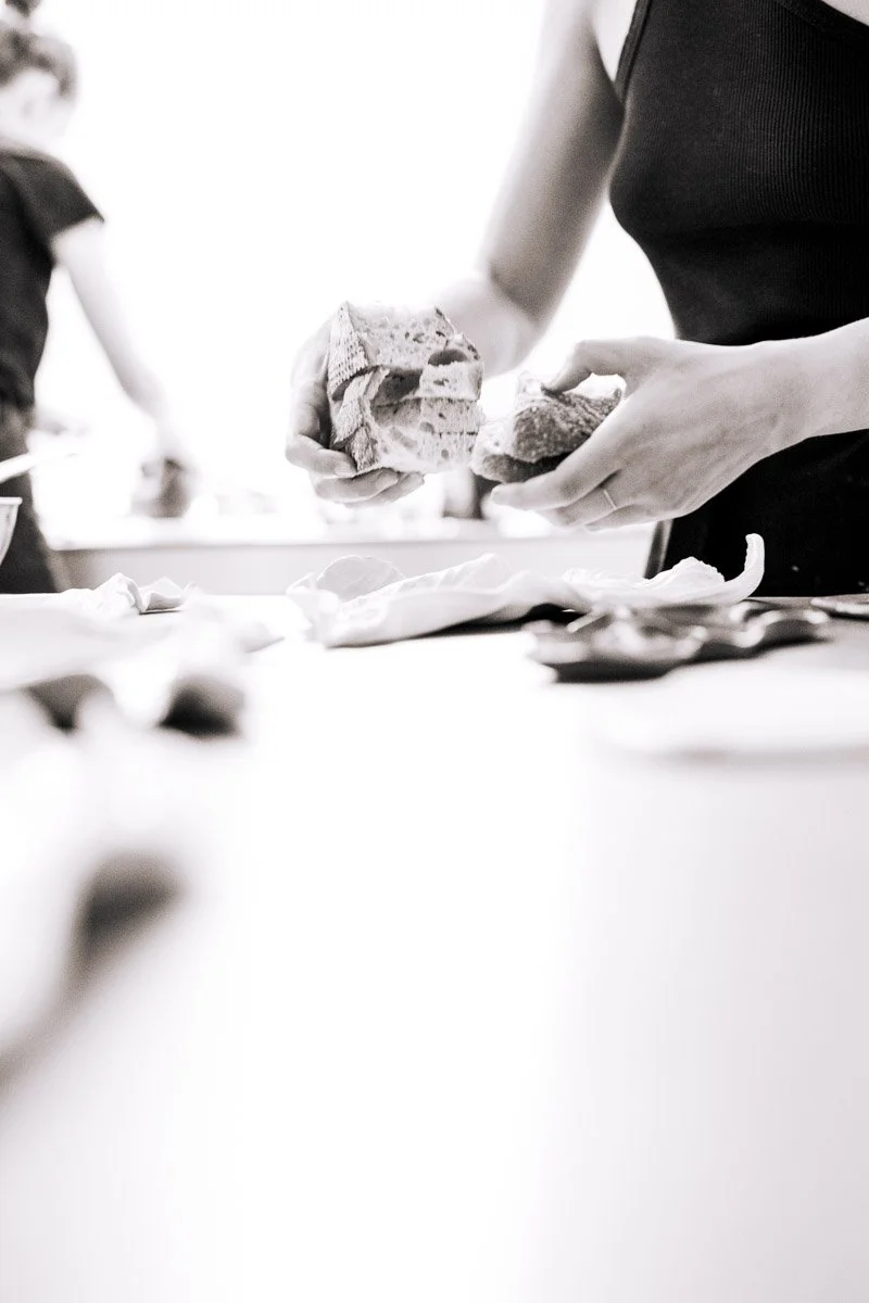 Person holding a loaf of bread in one hand and tearing a piece off with the other hand.