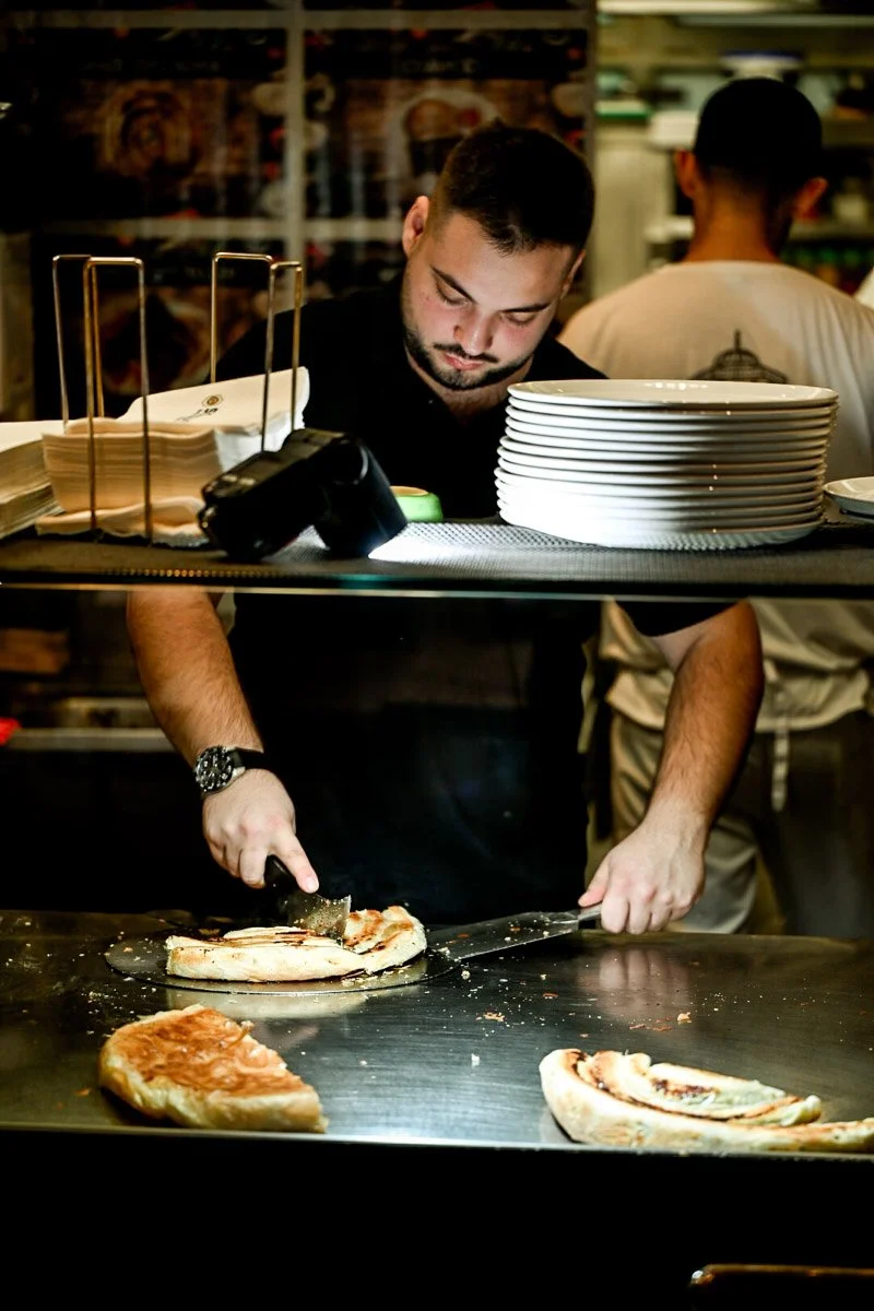 A pizza chef preparing pizza slices behind the counter in a restaurant kitchen.