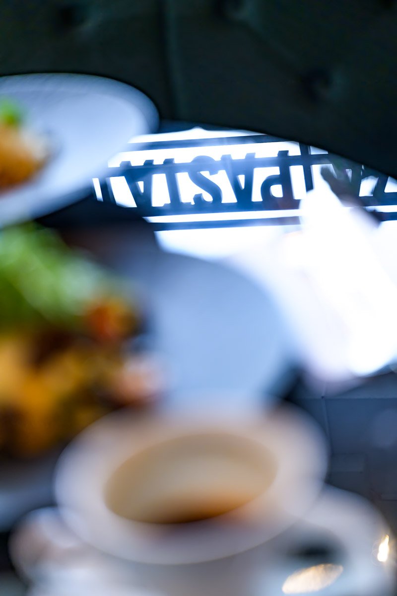 Blurred view of a Starbucks paper bag in a car, with a blurred coffee cup in the foreground and a plate of food on the side.