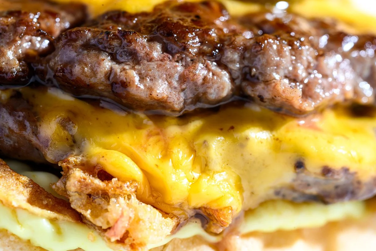 Close-up of a cheeseburger with melted cheese, beef patties, and bacon.