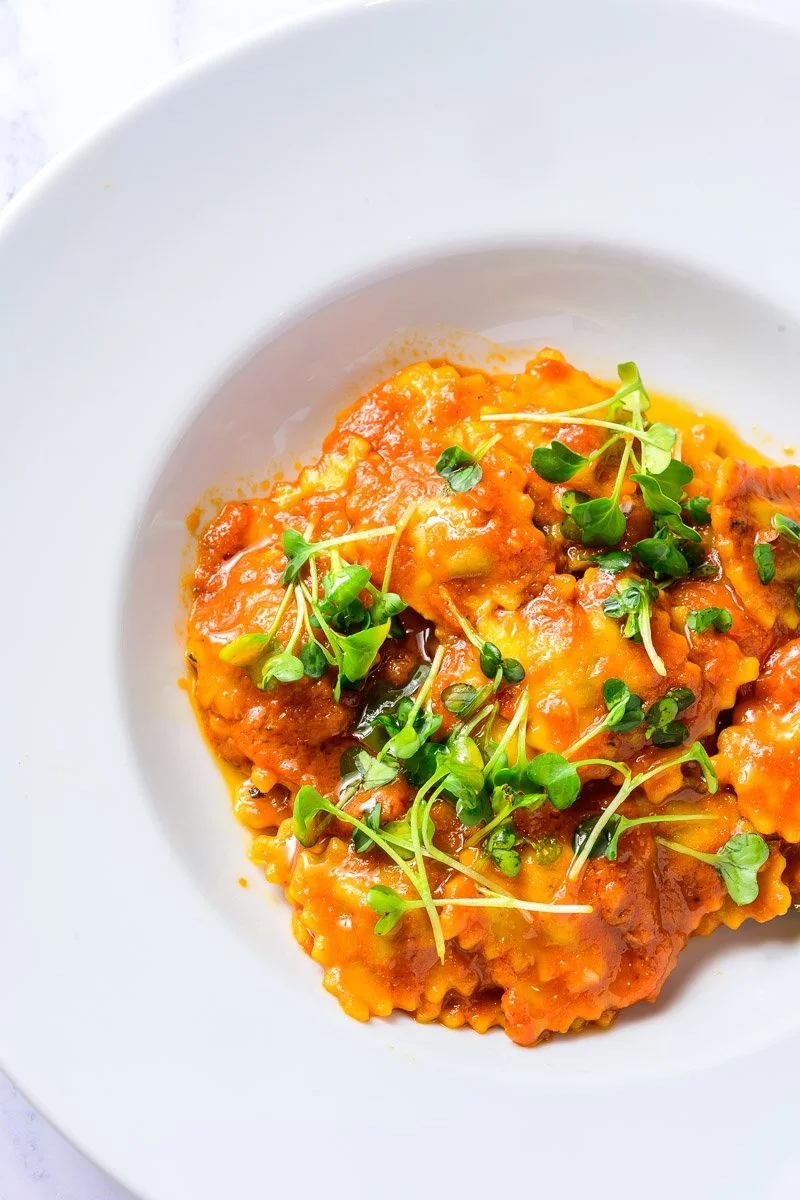 Plate of ravioli pasta topped with tomato sauce and garnished with microgreens.