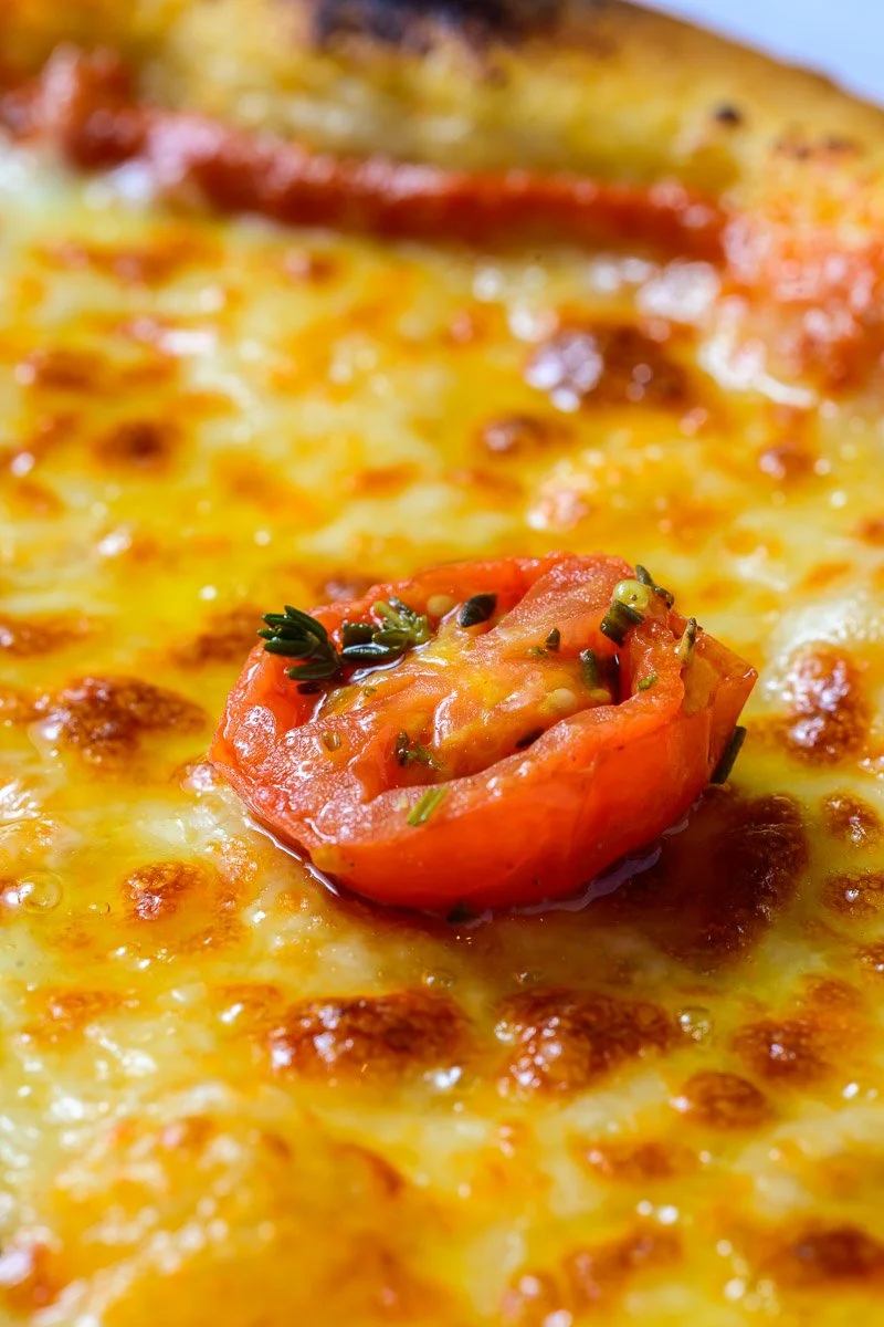 Close-up of a cheesy pizza slice with a cherry tomato garnish and herbs.