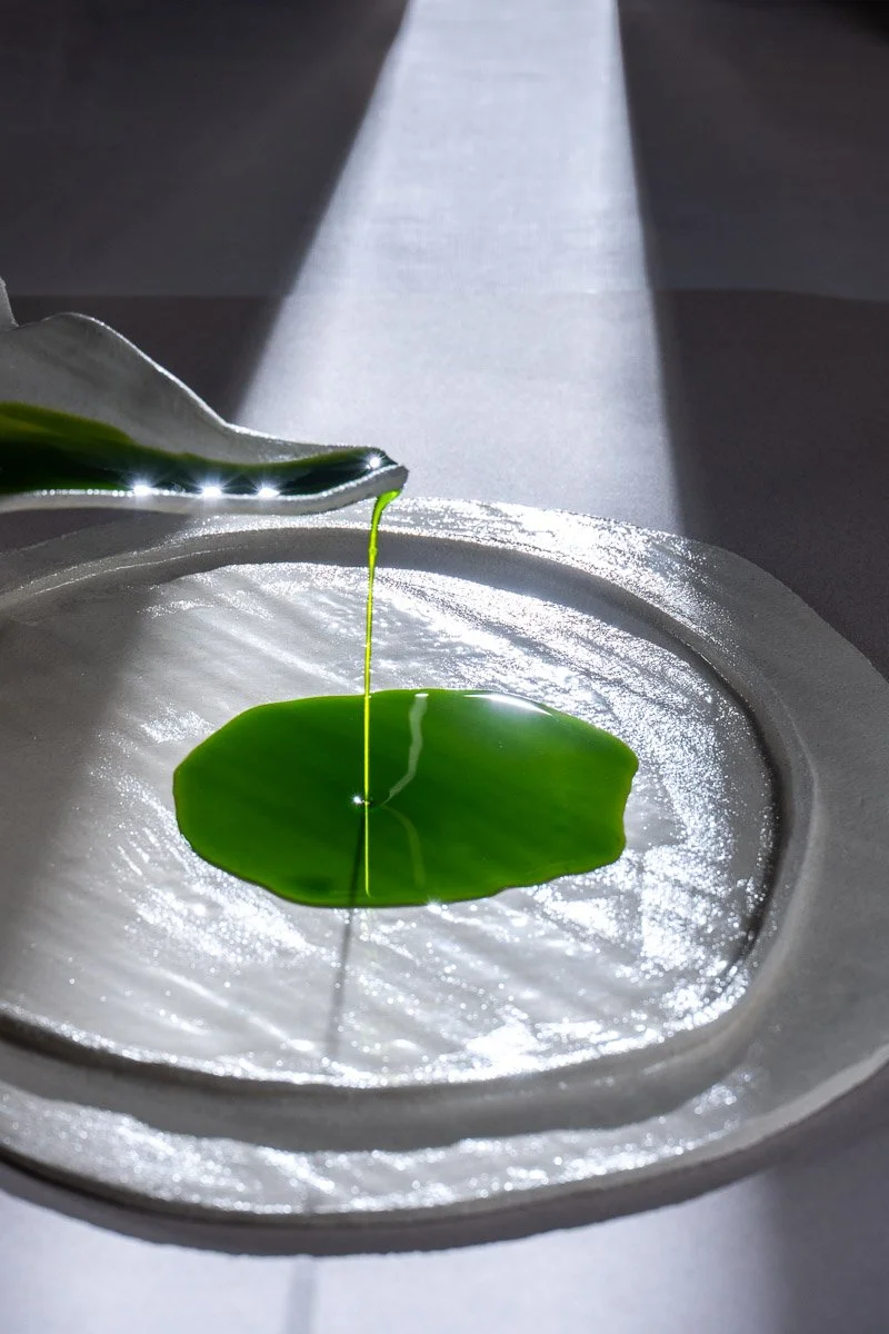 Pouring green liquid onto a white plate with a curved rim under sunlight.