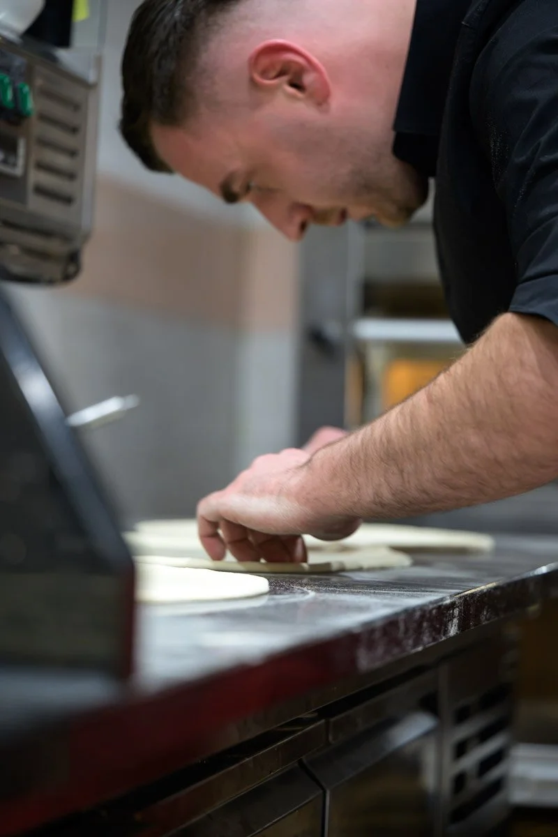 A man preparing pizza dough in a kitchen.