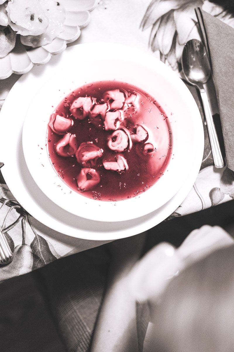 A white bowl of cooked octopus in red sauce on a table with a silver spoon and napkin nearby.