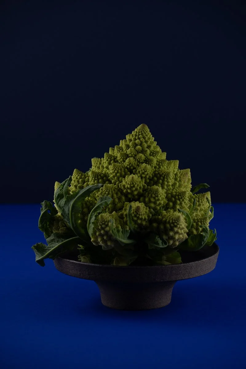A Romanesco broccoli with light green, spiral-shaped florets in a black bowl against a dark background.
