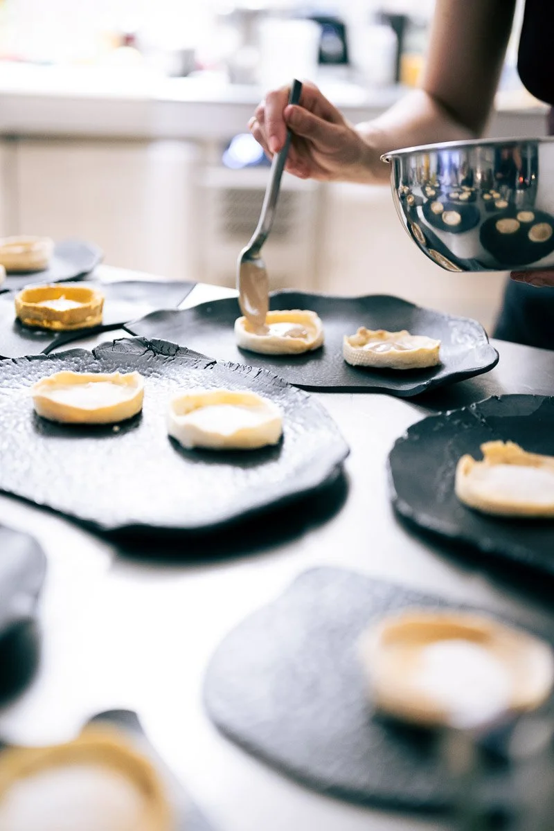 A person preparing to make mini cheesecakes or dessert cups by adding topping on small round pastry shells in a modern kitchen.