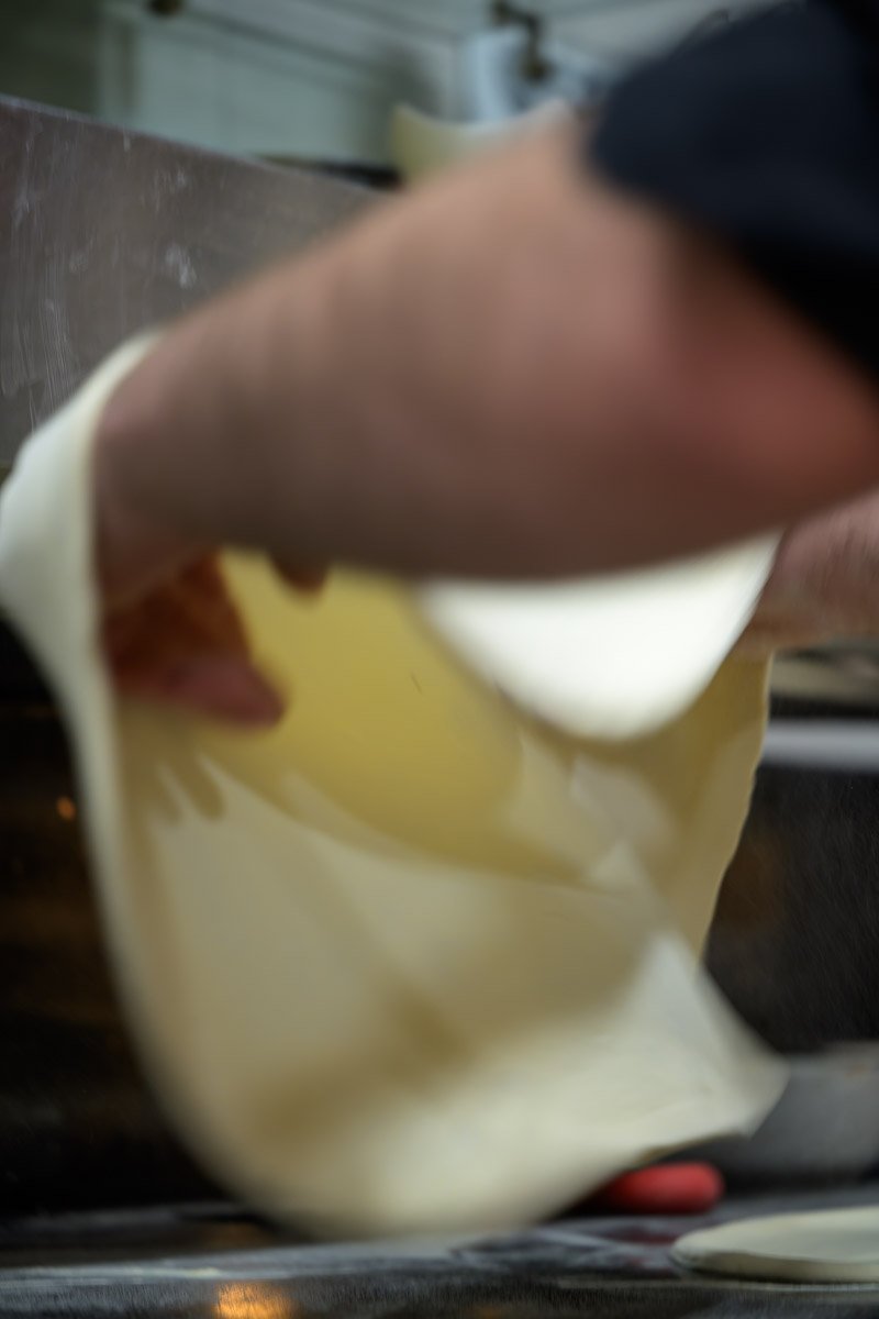 Close-up of a person's hand pouring yellow liquid, possibly batter or custard, into a pan or baking dish.