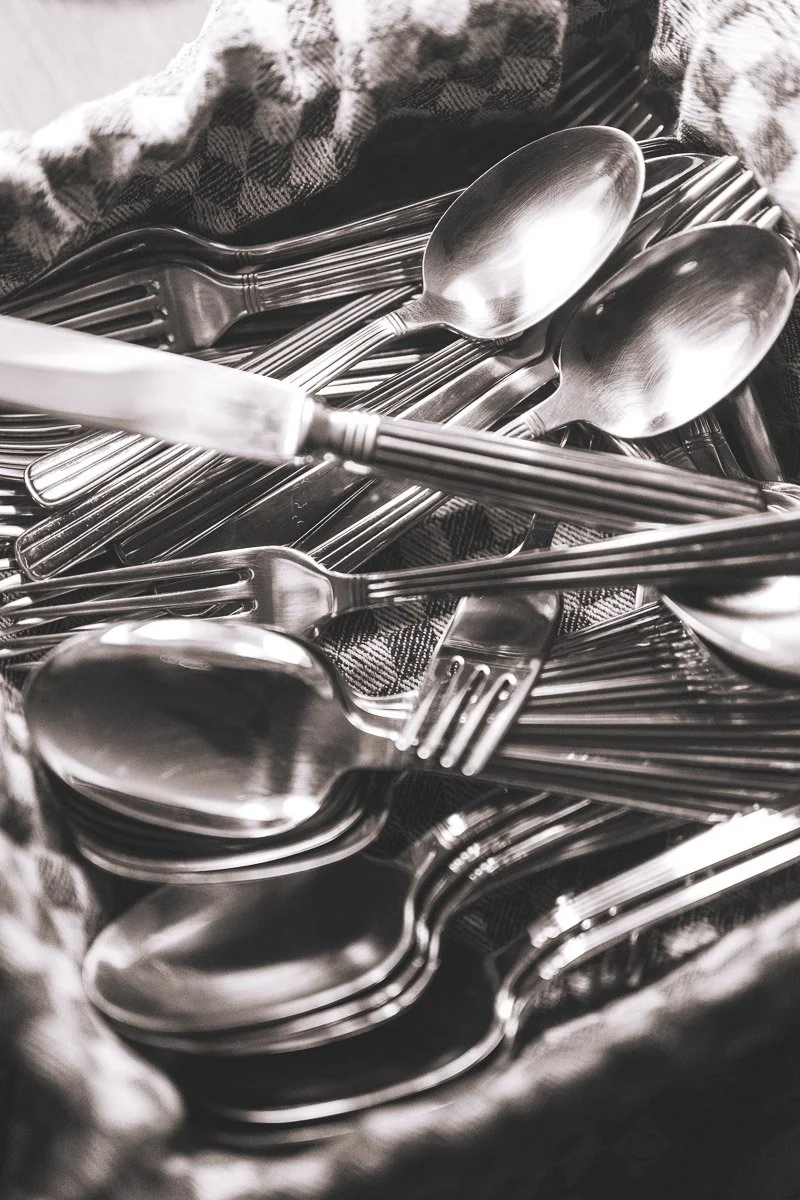 A collection of stainless steel spoons and forks arranged together, resting on a checkered cloth.