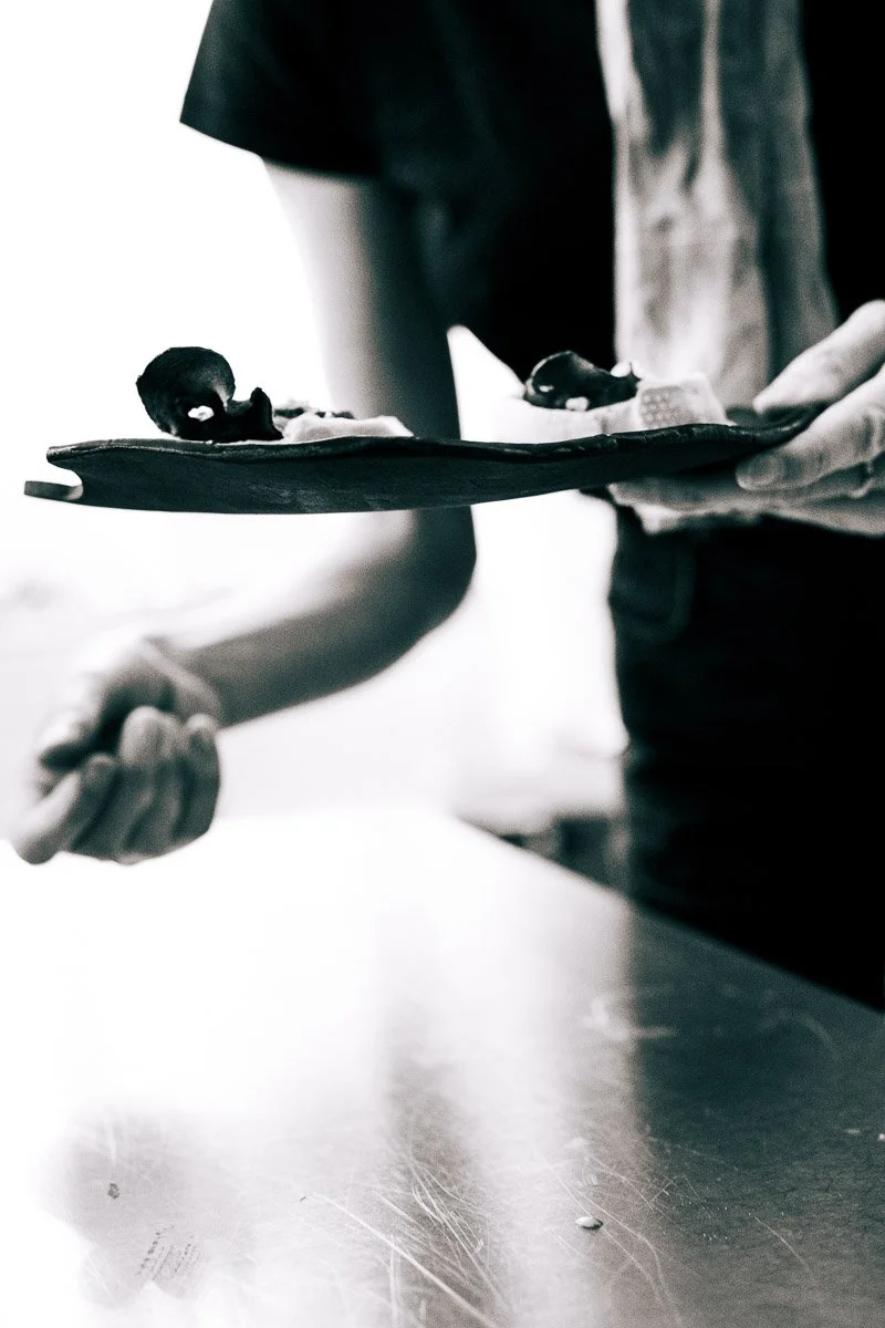 Close-up of a person holding a black dish with two tiny newborn babies wrapped in blankets, one with dark hair and the other with lighter hair, in black and white