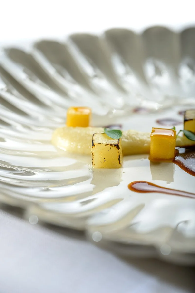 Close-up of gourmet dish with grilled cheese cubes, greens, and sauces on a decorative silver platter.