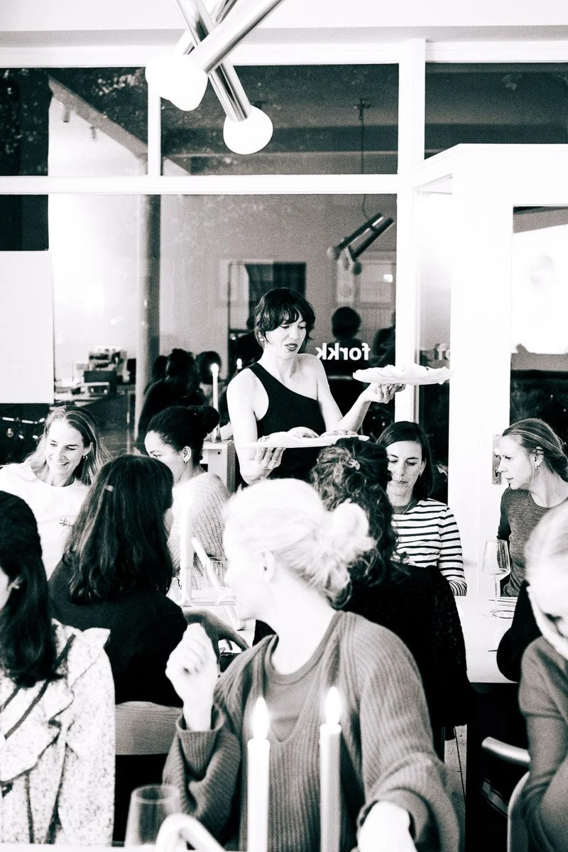 A woman serving food at a restaurant with patrons dining at tables, candles, and wine glasses.