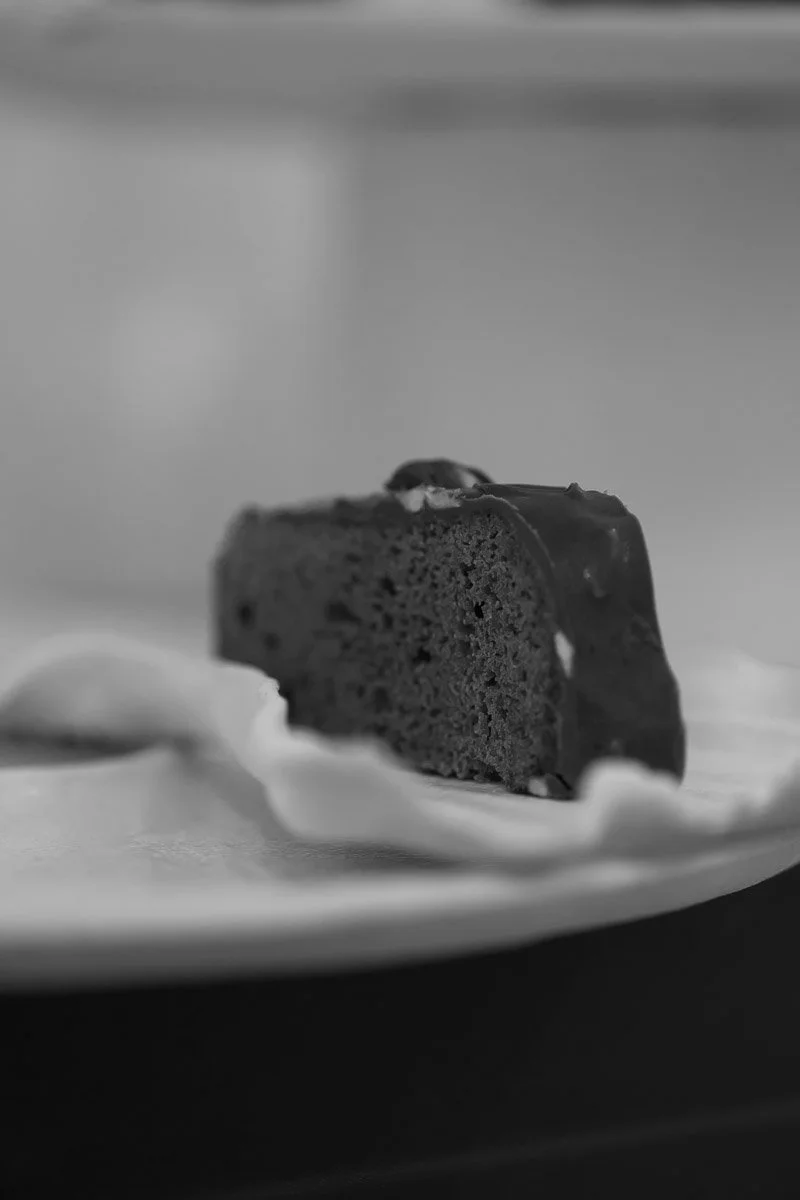 A slice of chocolate cake with icing on top, placed on a white plate.