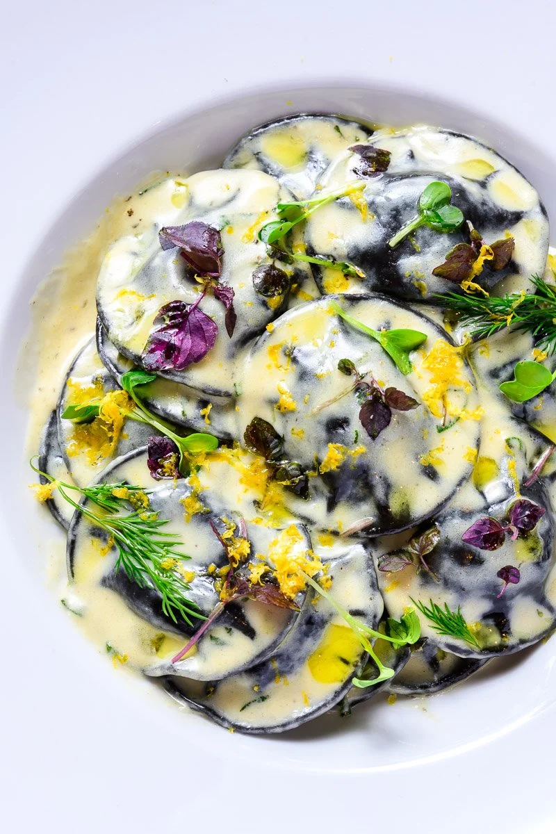 Eggplant slices topped with a creamy sauce, garnished with fresh herbs and edible flowers.