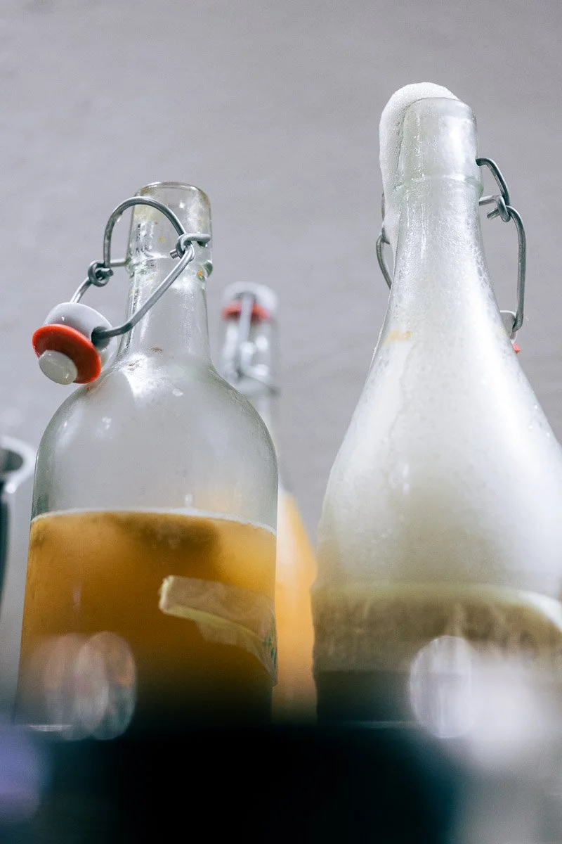 Close-up of two glass bottles with flip-top stoppers, one containing a brownish liquid and the other with a frosted appearance, against a gray background.