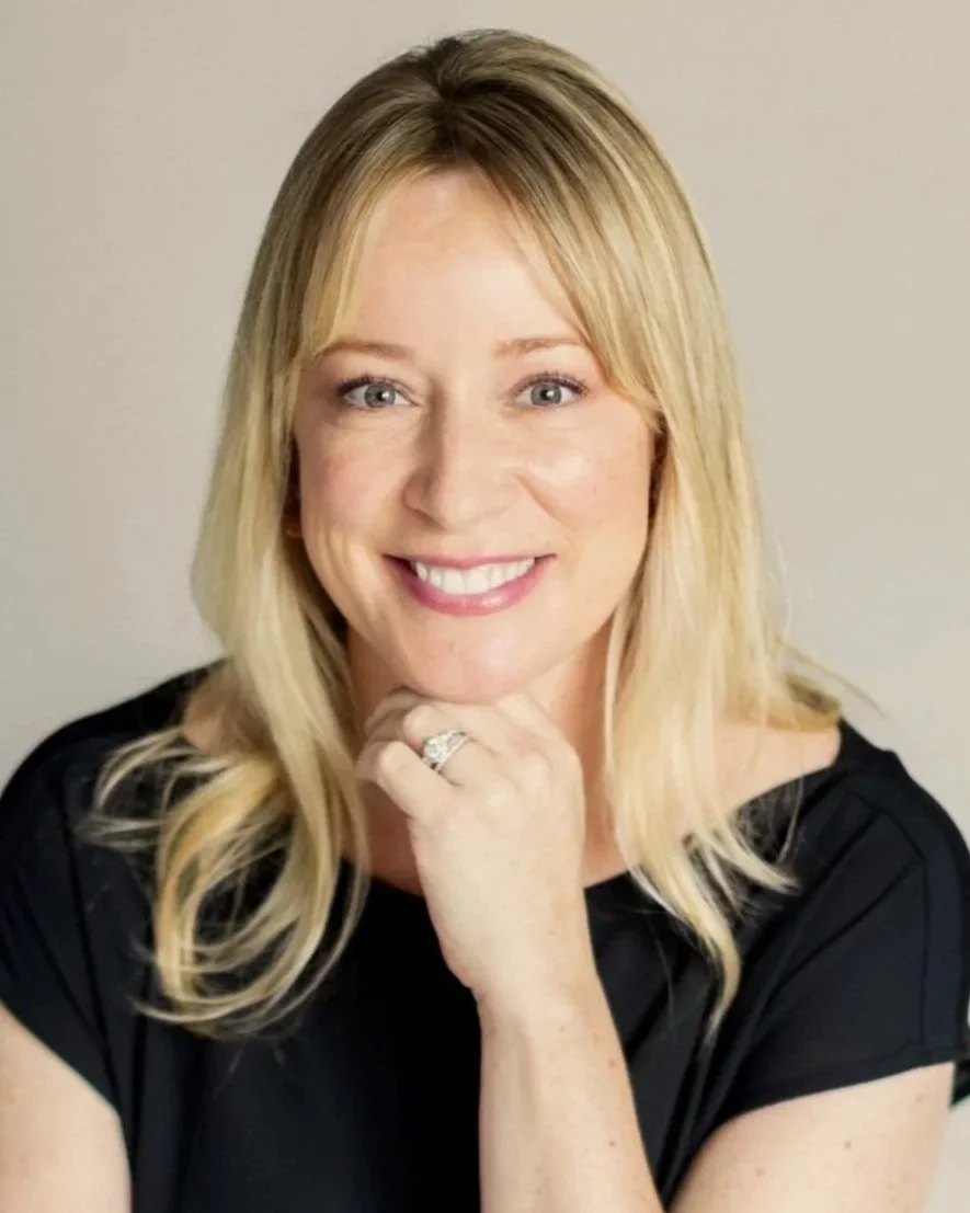 Portrait of K. Ashley Hoffman, MEd, LPC, a woman with blonde hair, smiling, wearing a black top, and resting her chin on her hand with a ring.
