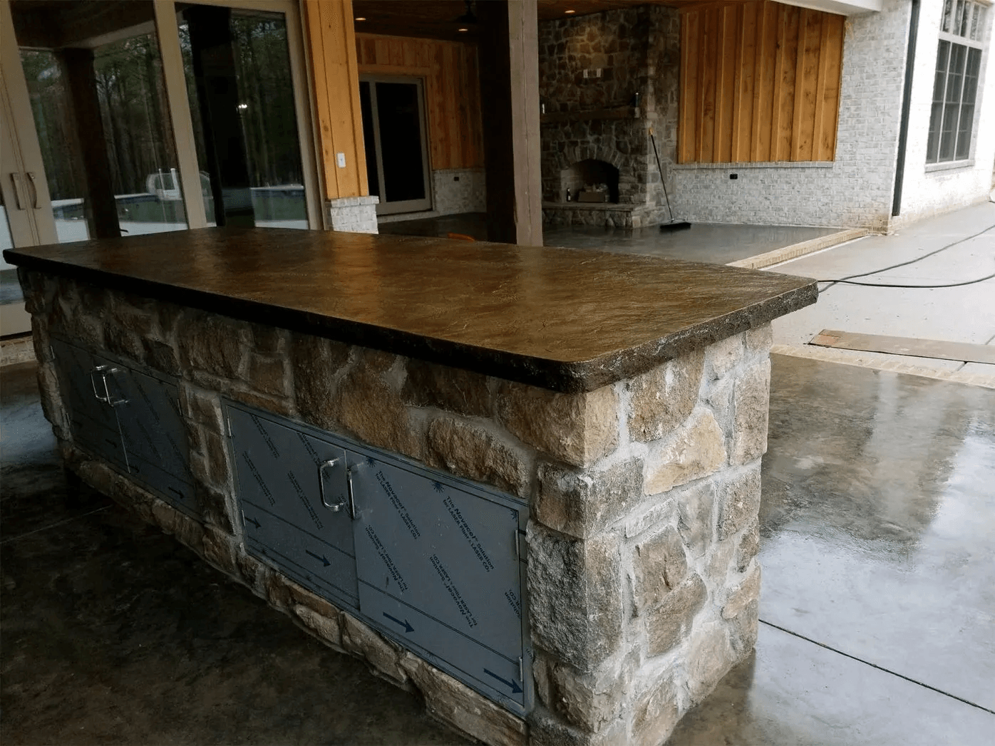 Stone kitchen island with a dark wood countertop in an indoor-outdoor space under construction.