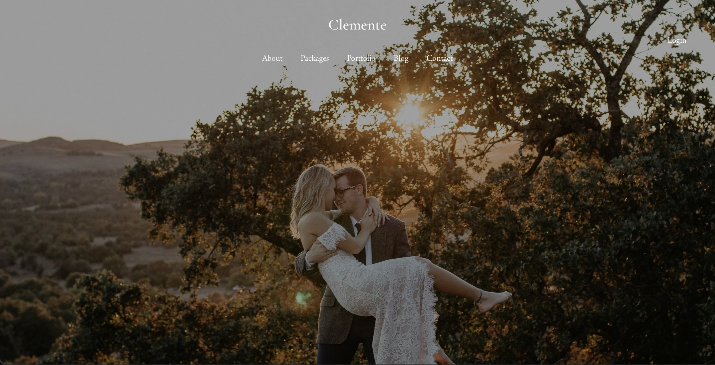 A couple, the woman in a white lace dress and the man in a suit, embracing under a large tree during sunset.