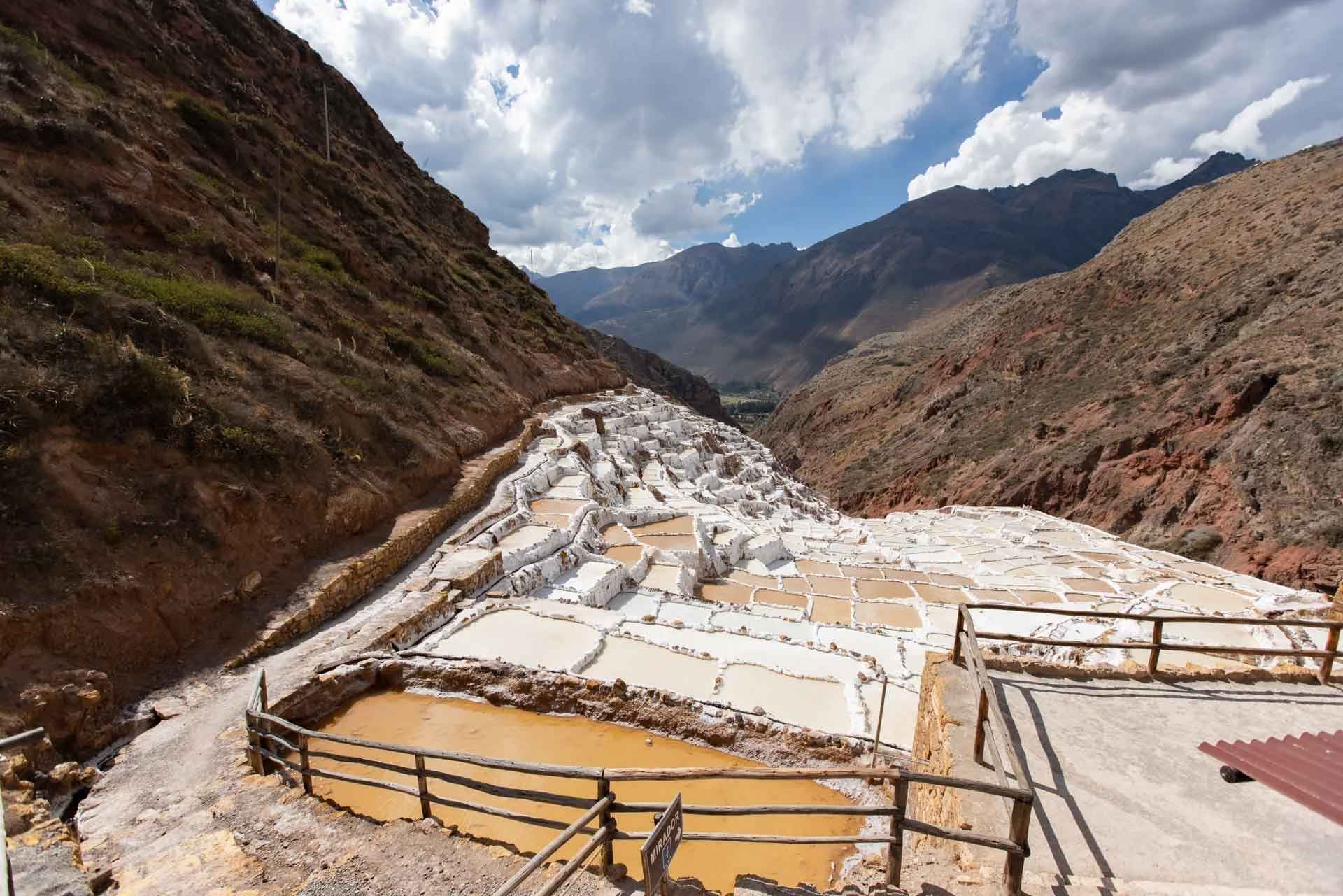Salt terraces in a mountainous landscape with clouds in the sky.