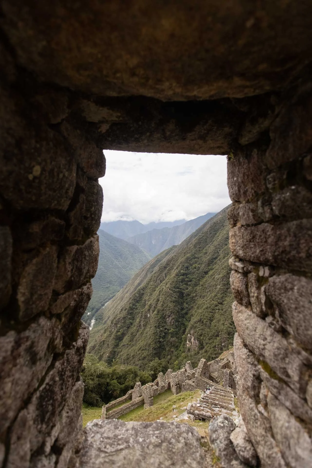 View through a small stone window at Machu Picchu showing lush green mountains and ancient ruins.