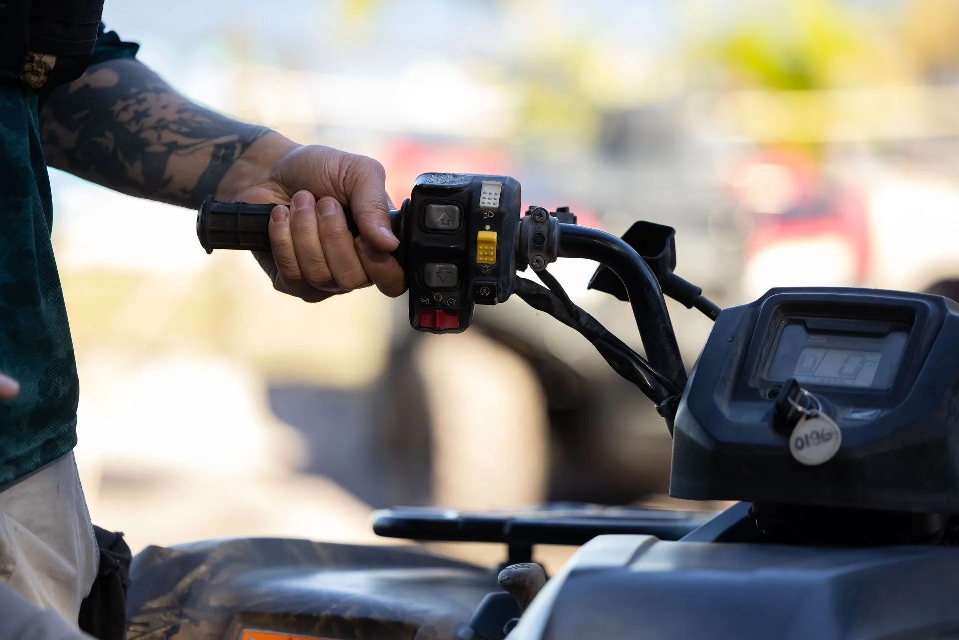 A person holding the handlebar of an all-terrain vehicle (ATV) with their left hand, showing the ATV's control panel and various buttons.