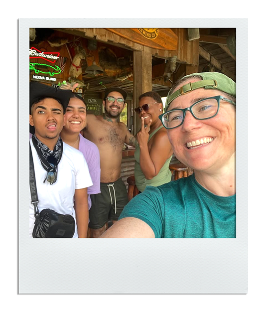 Group of five friends smiling and posing for a selfie inside a rustic bar or restaurant with wooden decor.