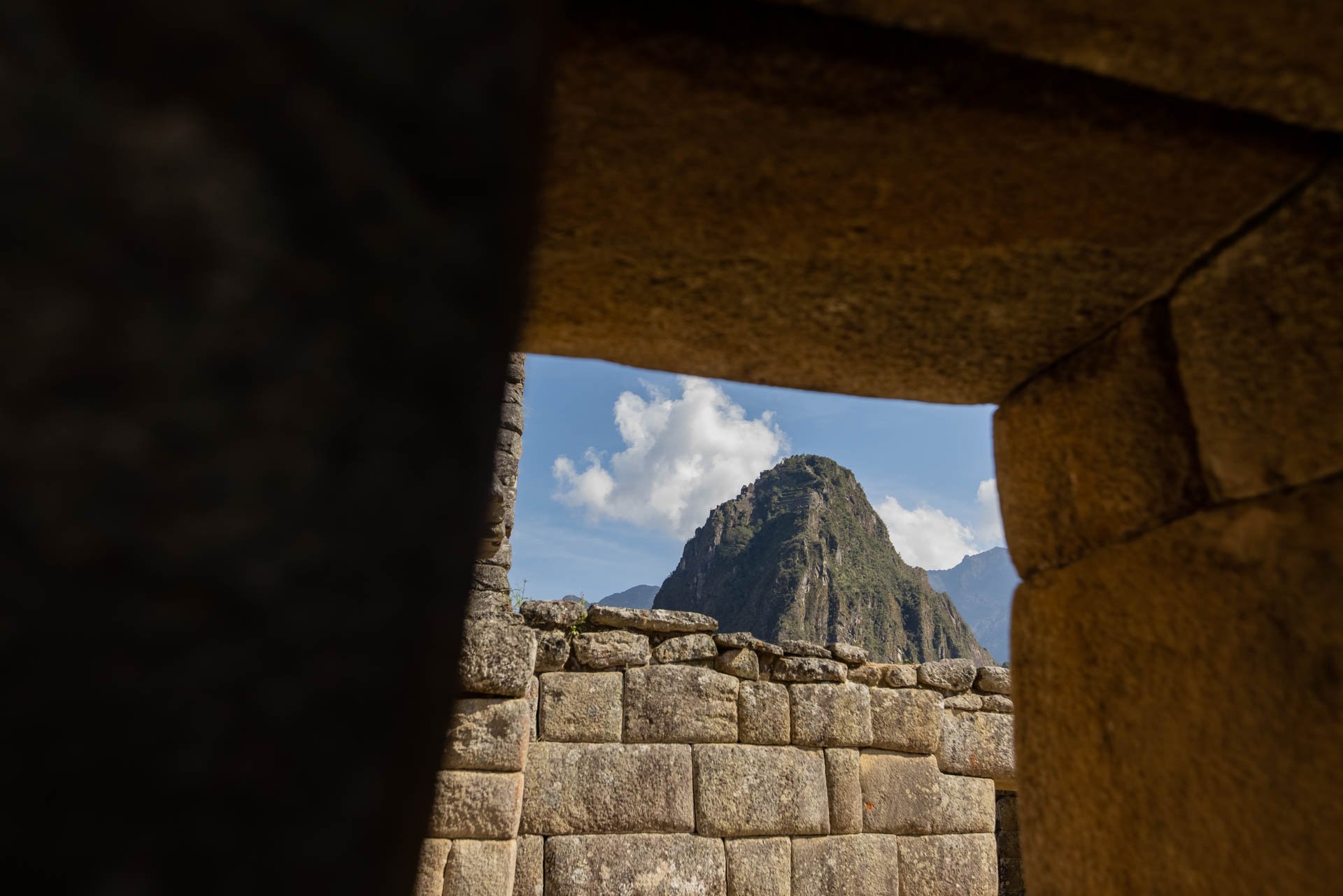 View of a mountain through the stone structure of Machu Picchu, with a partly cloudy sky in the background.