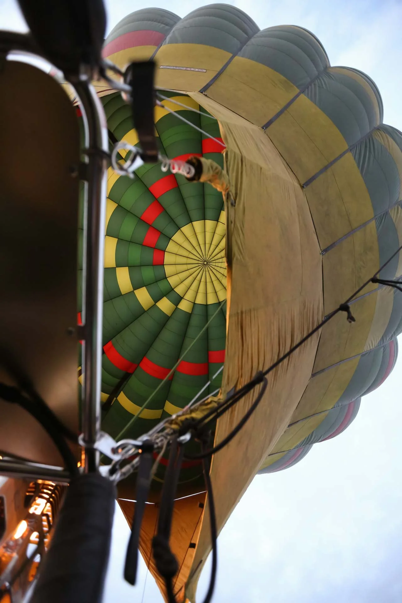View from inside a hot air balloon basket looking up at the colorful balloon canopy with yellow, green, and red sections against the sky.
