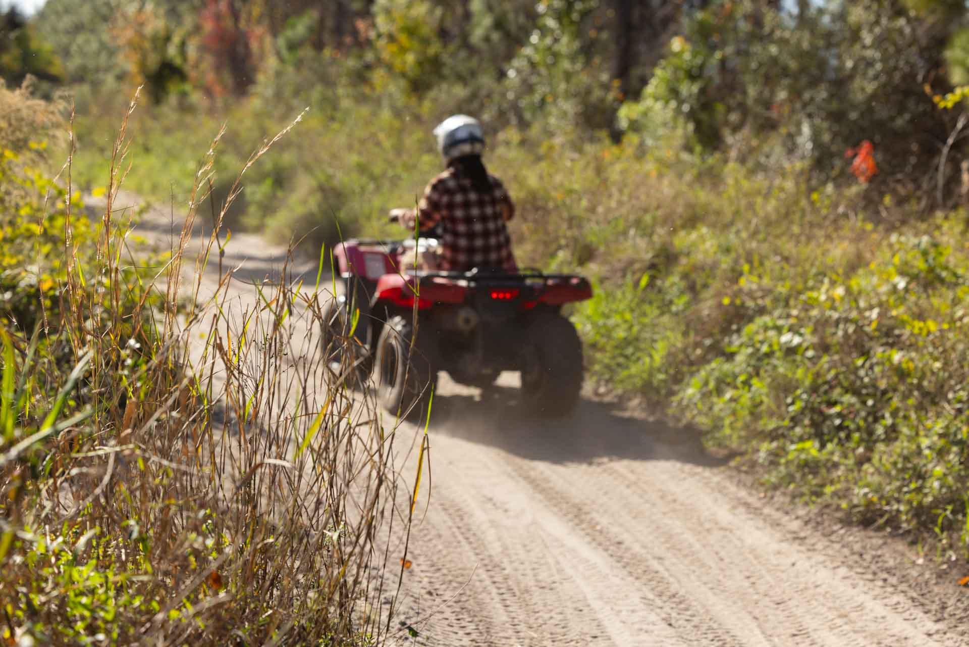 A person riding an all-terrain vehicle (ATV) on a dirt trail surrounded by dense trees and foliage.