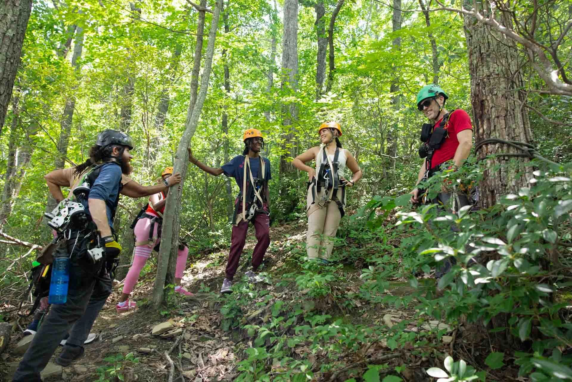 Group of five people with helmets and harnesses preparing for a forest canopy activity surrounded by green foliage.
