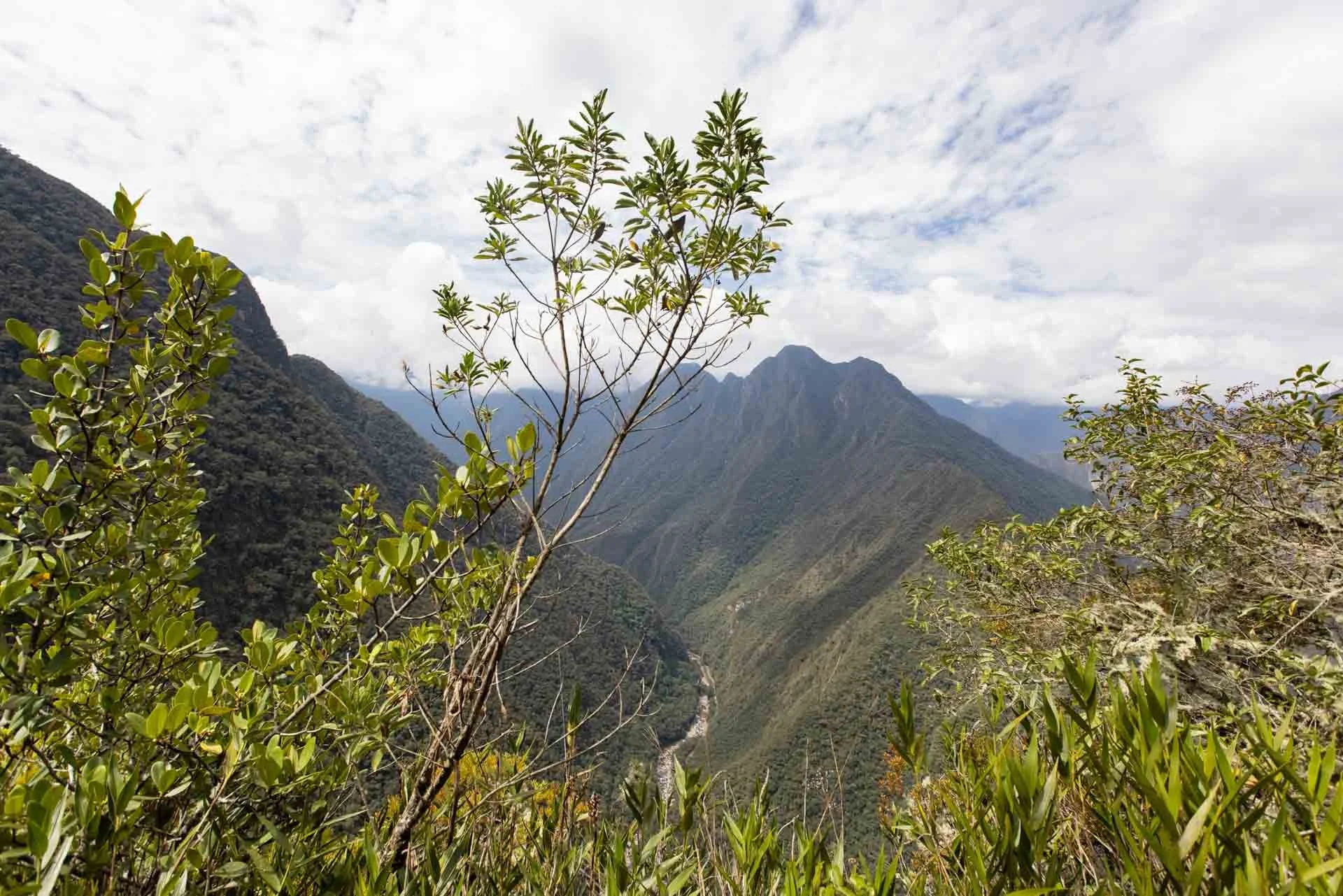 Mountains and valleys with green vegetation in the foreground, partially cloudy sky in the background.