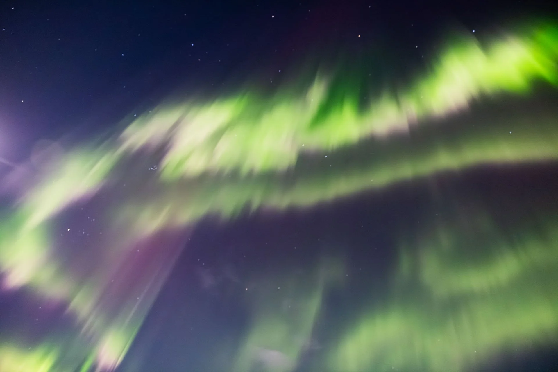 Blurred green and purple northern lights over the night sky with stars.