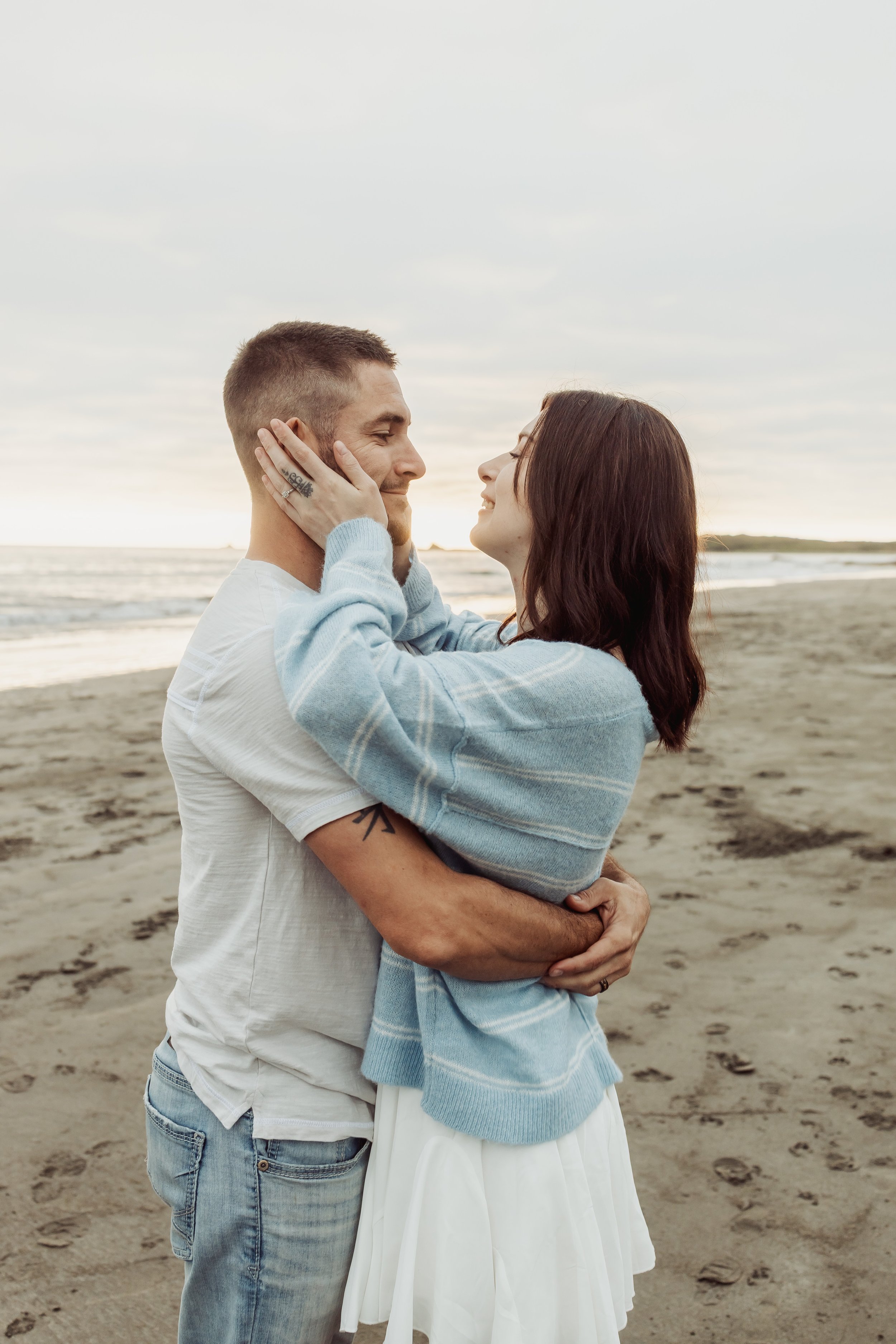 A couple embracing on a beach with the ocean in the background, smiling at each other.