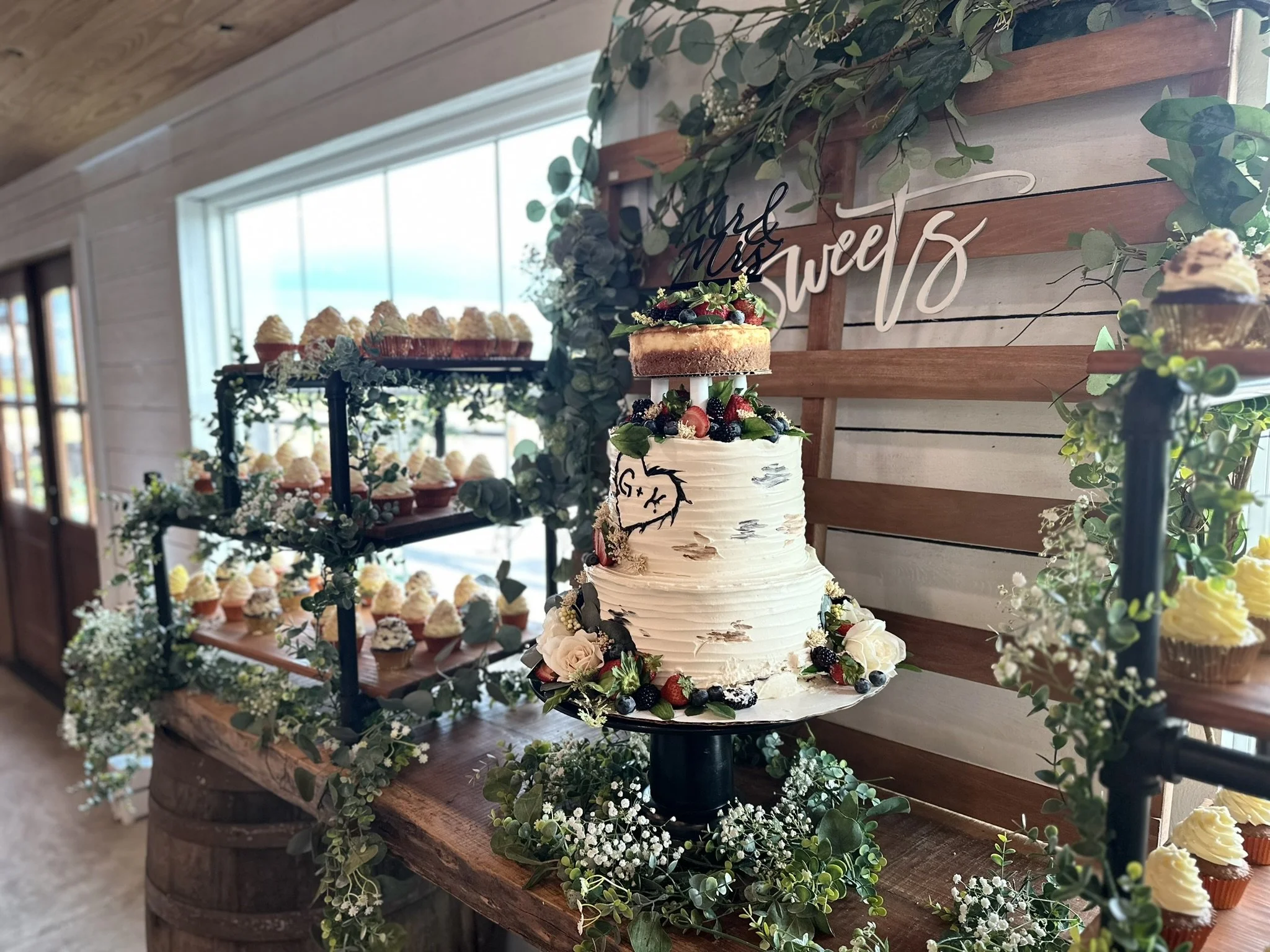 Cake and desserts on a custom live edge wood table with a sign that says sweets in the background.
