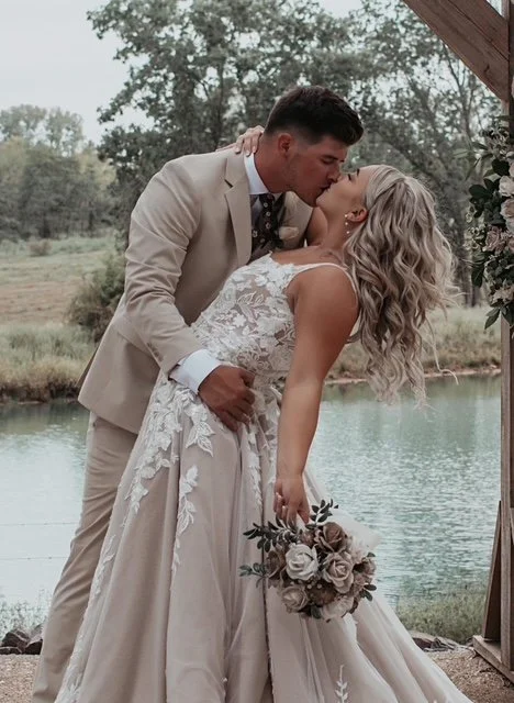 A couple kisses at Berkshire Ridge a wedding venue south of St. Louis in the forest ceremony area.  The bride's bouquet is hanging by her side with the other hand holding onto the groom's nape of his neck.  It looks like a fairytale.