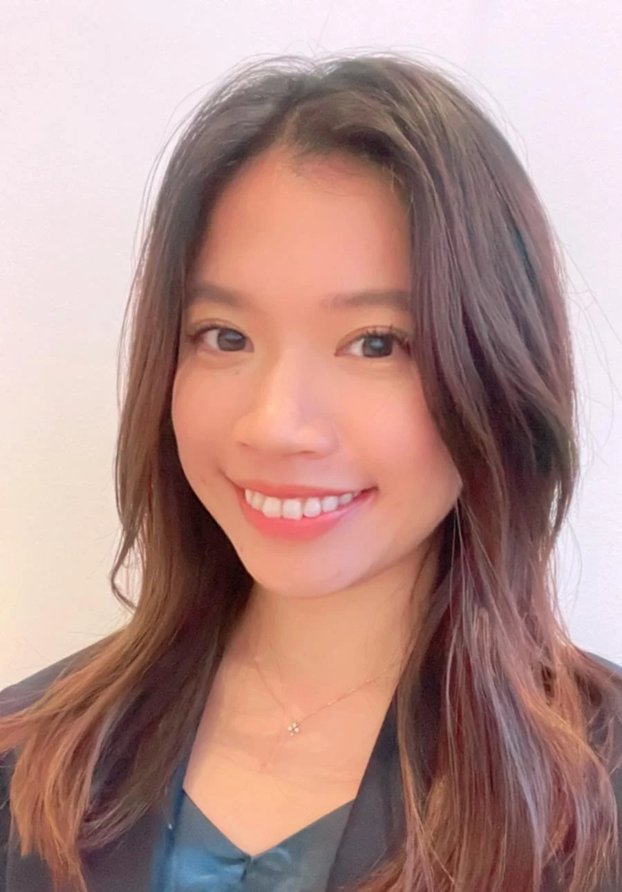 Smiling woman with long hair and dark blazer against a light background.
