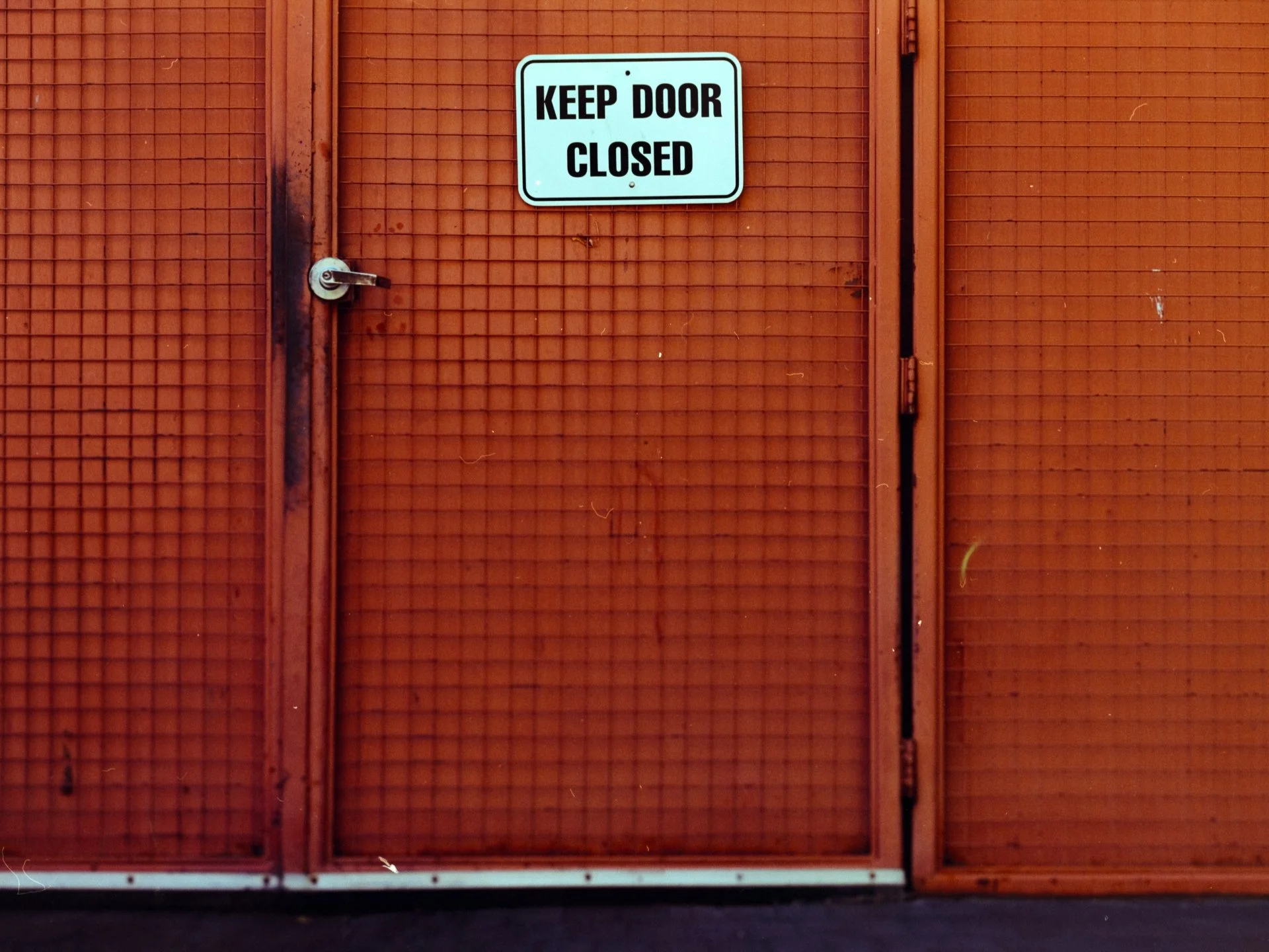 Orange industrial door with a sign that reads 'Keep Door Closed' and a small latch handle.
