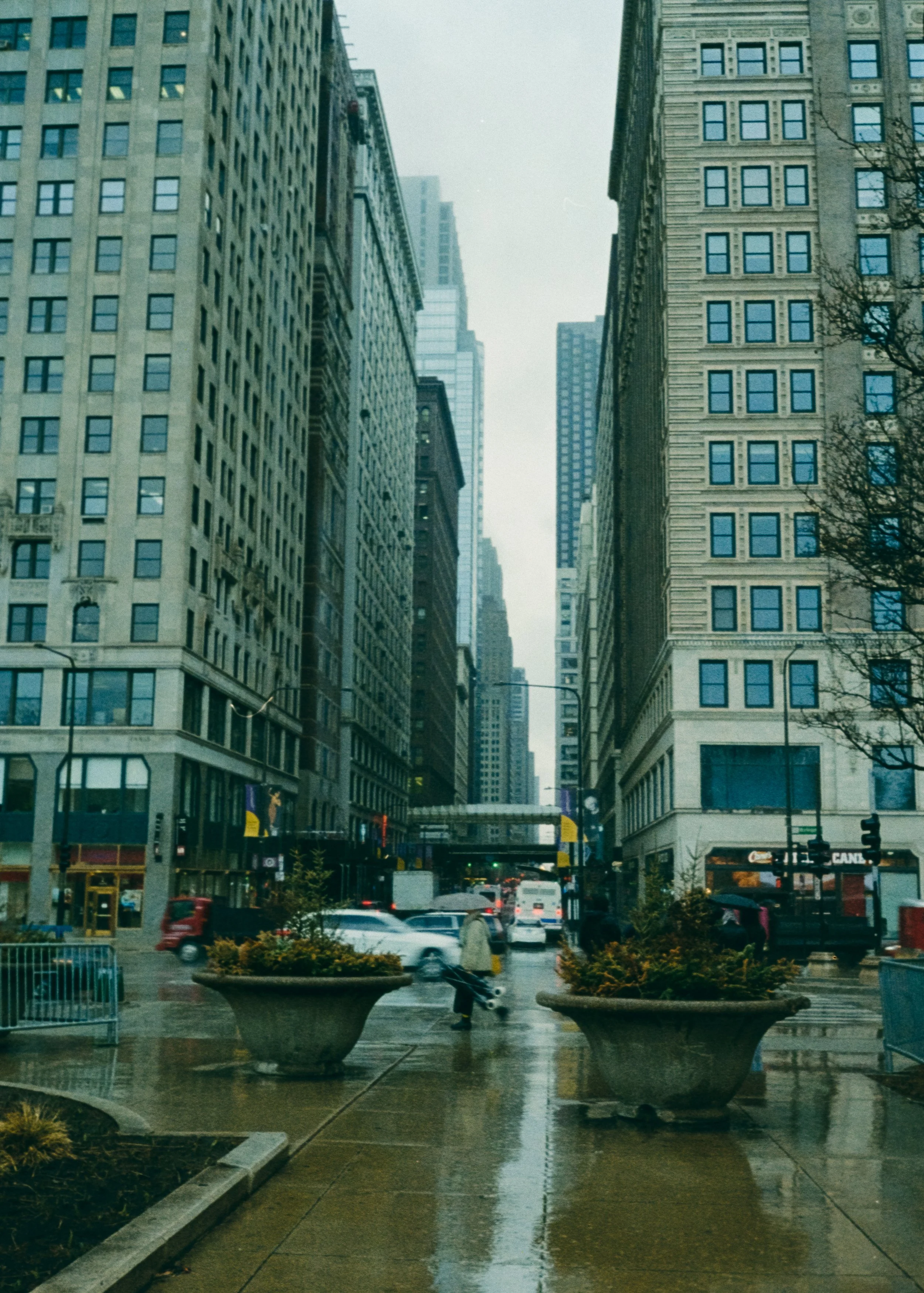 City street scene on a rainy day in downtown, with tall buildings, wet pavement, and few pedestrians.
