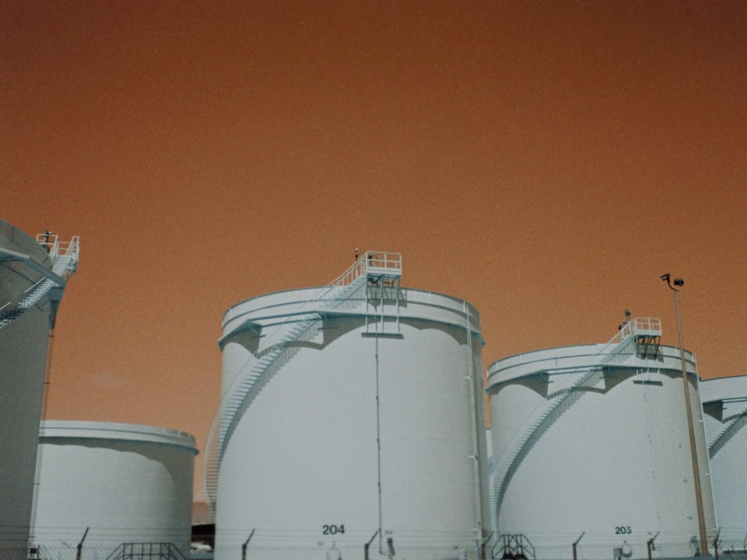 Industrial storage tanks against an orange sky.
