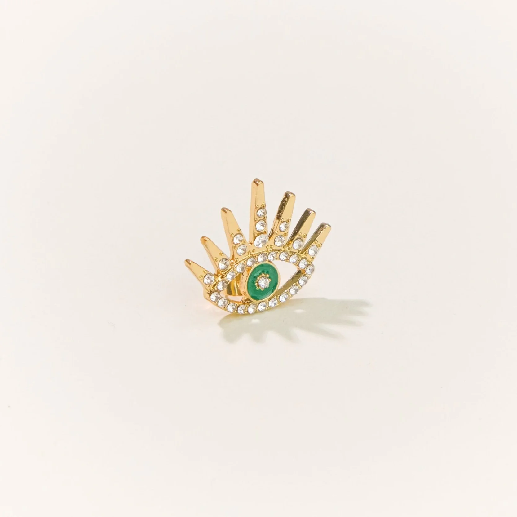 Anillo dorado con diseño de ojo, adornado con cristales blancos y un centro en color verde.